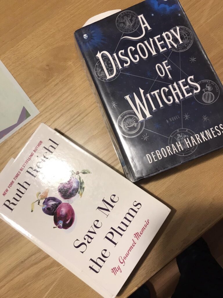 (Image is of two books on a desktop. The titles are Save Me the Plums and A Discovery of Witches)