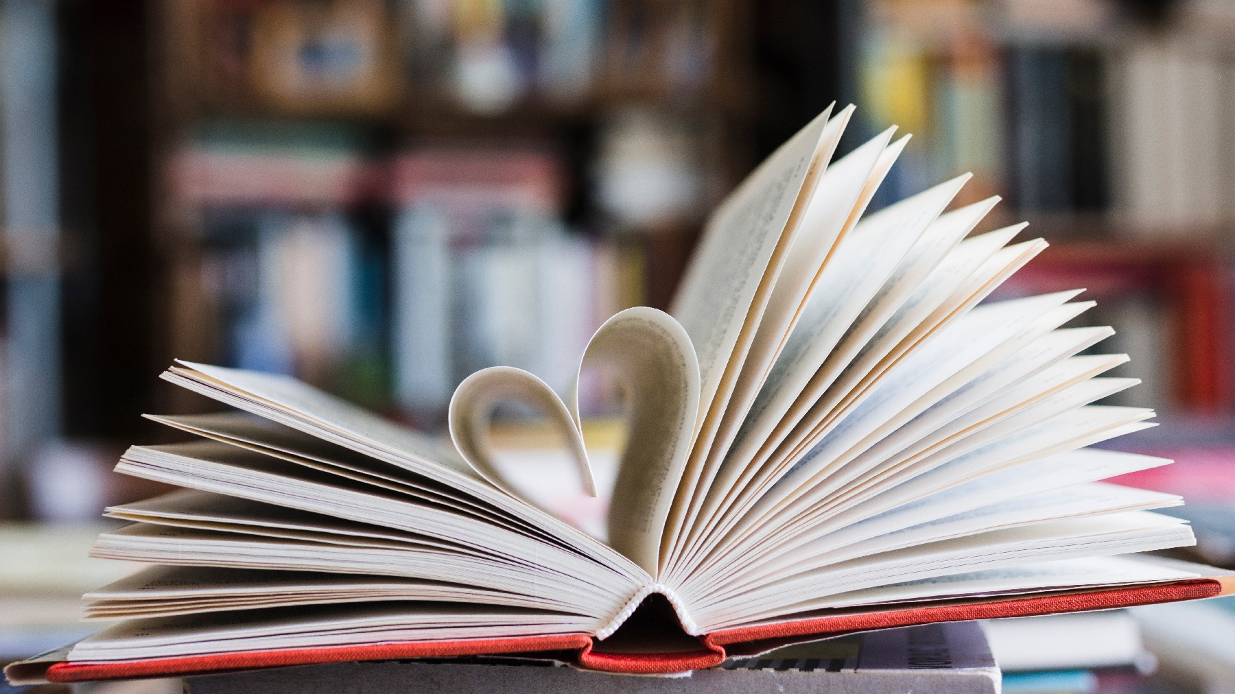 An open book on a table with the pages forming a heart in a library.